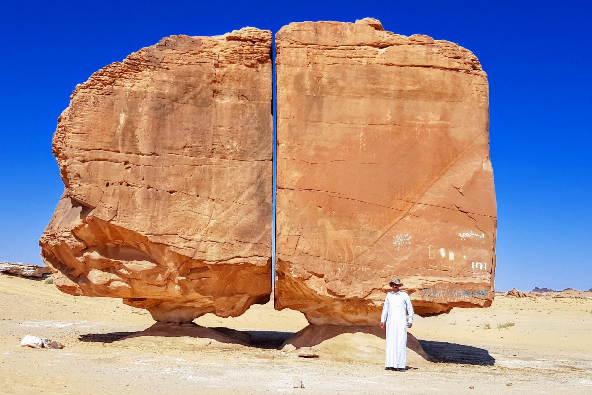 صخره النصله در جنوب شهر تیما در عربستان سعودی و مرد عرب با دشداشه در سمت راست صخره