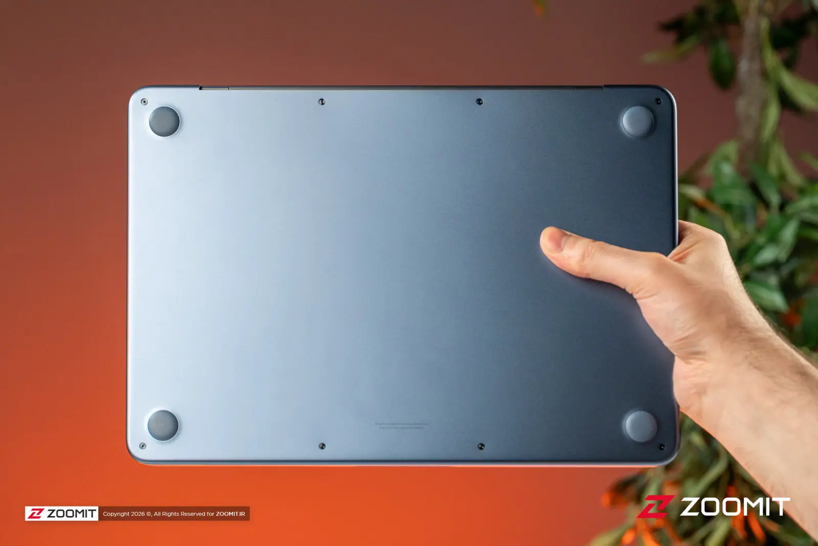 بدنه زیرین لپ‌تاپ مک بوک نئو (MacBook Neo) در دست یک فرد