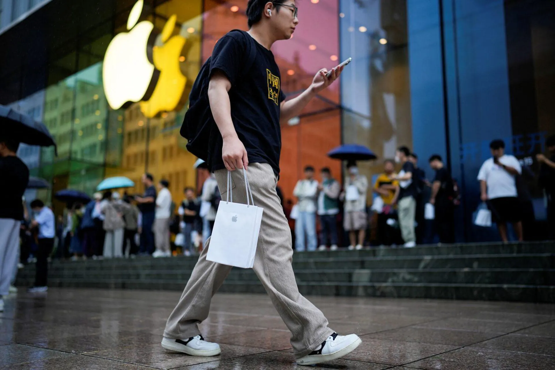 مرد چینی درحال عبور از خیابان با کیسه خرید اپل با زمینه فروشگاه اپل