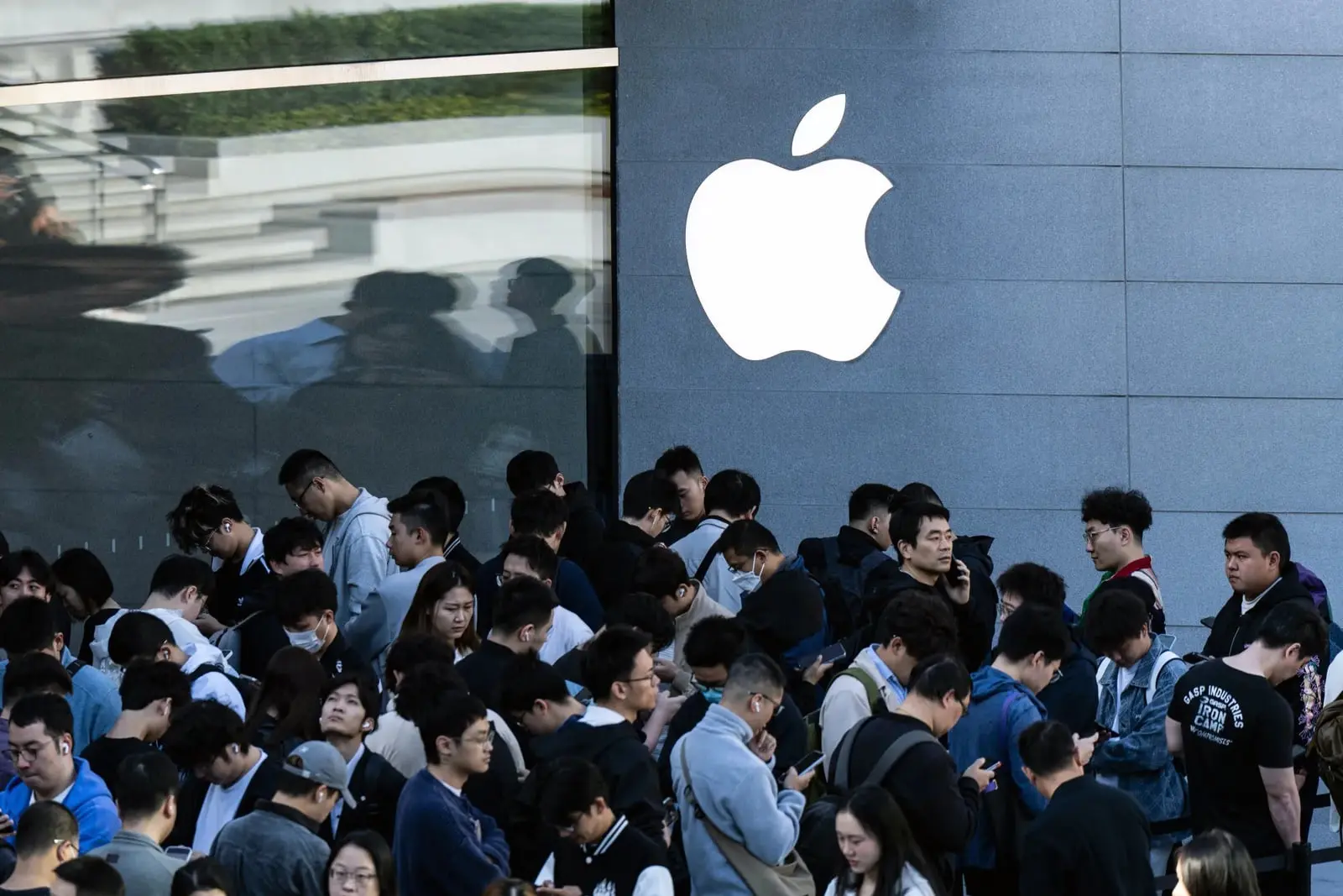 لوگوی اپل (Apple) روی دیوار فروشگاه در کنار جمعیت مشتریان
