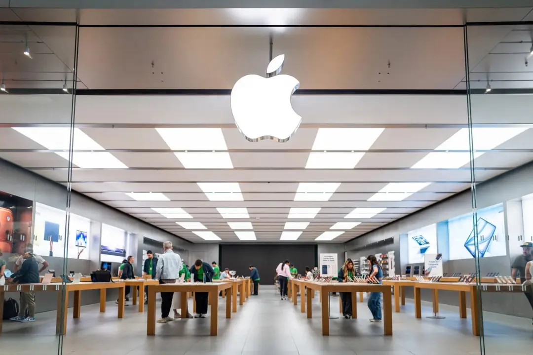 نمای داخلی فروشگاه اپل (Apple Store) با میزهای نمایش محصولات و مشتریان