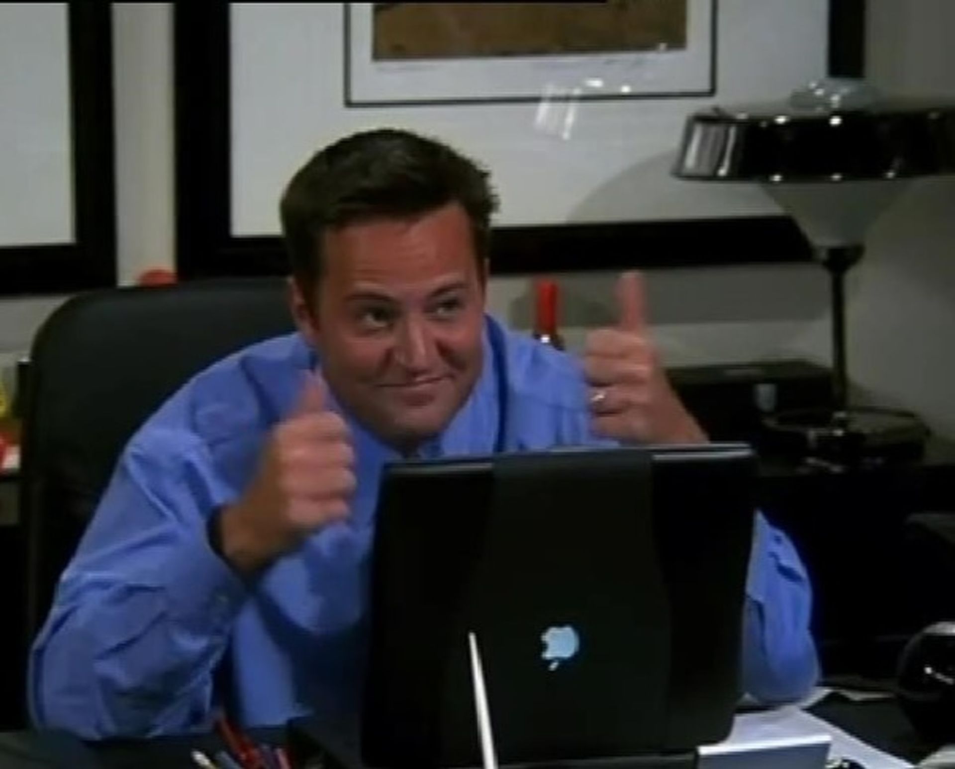 یک مرد با لباس آبی و لبخندزنان پشت لپ‌تاپ اپل