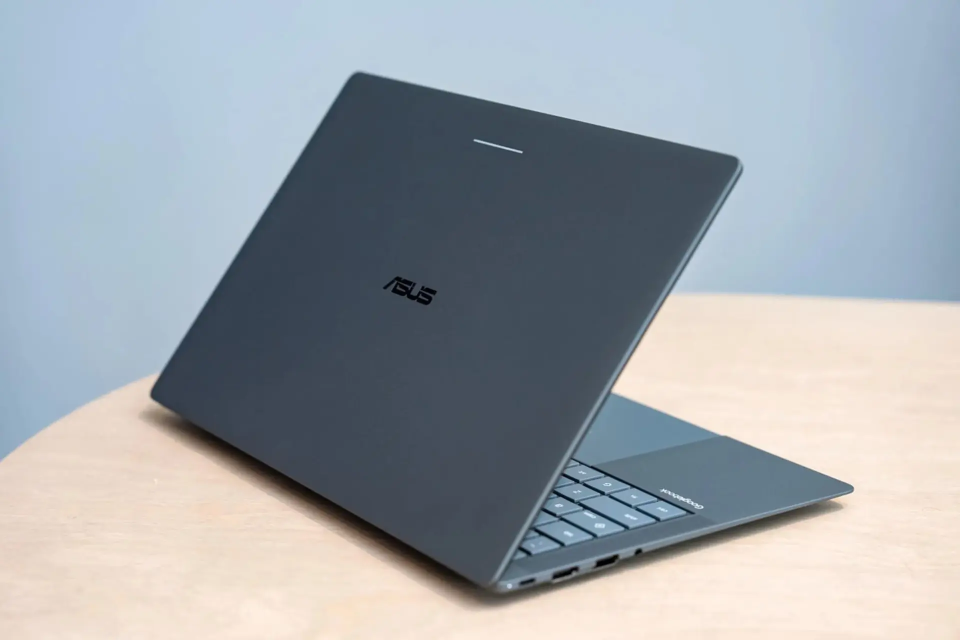 لپ‌تاپ ایسوس (ASUS) با بدنه خاکستری روی میز چوبی
