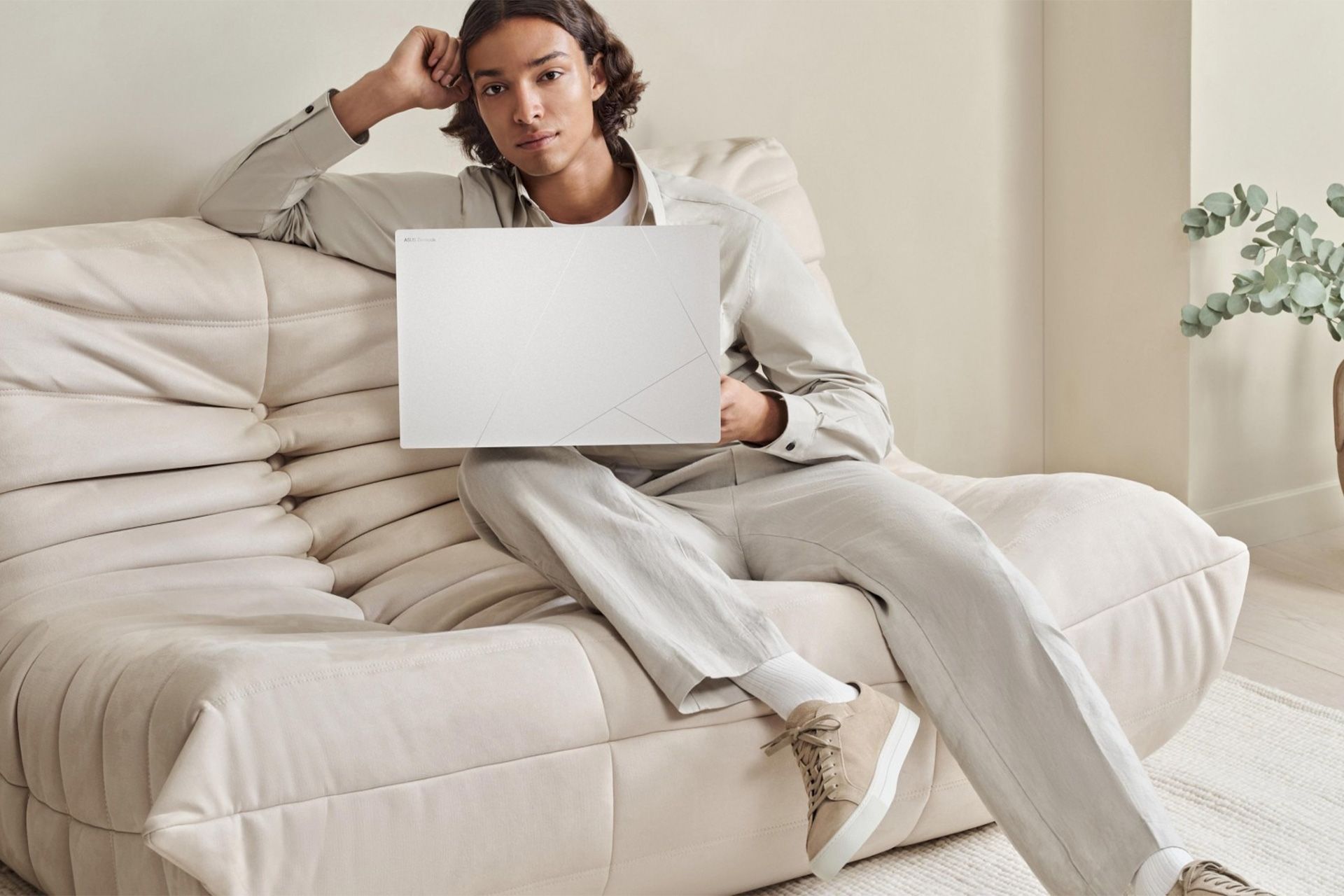  لپ‌تاپ ایسوس Zenbook S16 روی پای یک مرد نشسته روی مبل