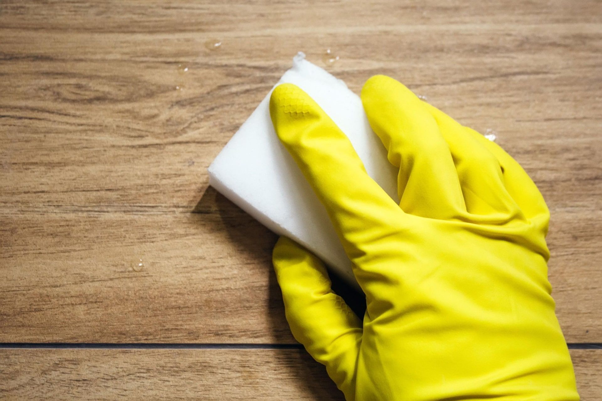 دستکش پلاستیکی زرد در حال تمیز کردن سطح چوبی با اسفنج سفید
