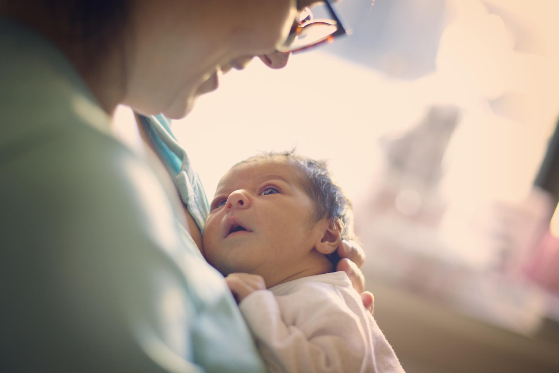 نوزاد کوچکی در بغل یک خانم به سینه‌اش چسبیده و به صورت زن نگاه می‌کند