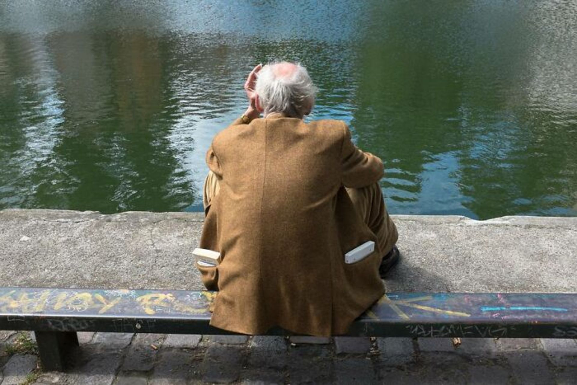 پیرمرد تنها روی نیمکت لب دریاچه دو کتاب در جیب کت