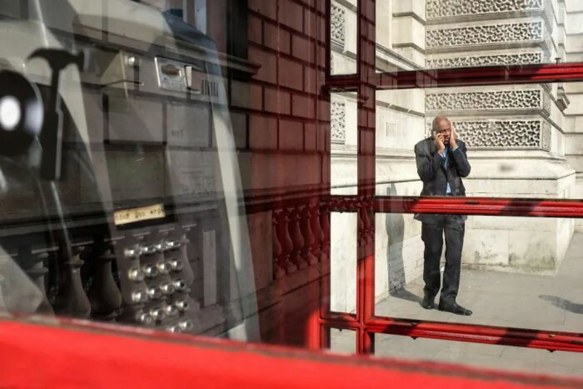 مرد در حال مکالمه با تلفن در پشت باجه تلفن قرمز