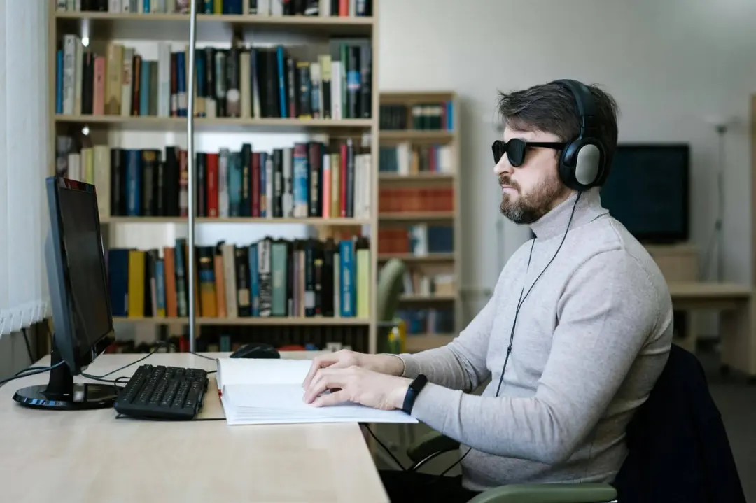 مرد نابینا (Visually Impaired) با هدفون و عینک سیاه در حال کار با کامپیوتر