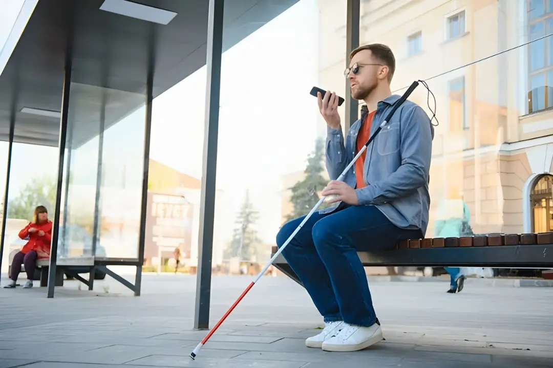 مرد نابینا با عصای سفید در ایستگاه اتوبوس نشسته است