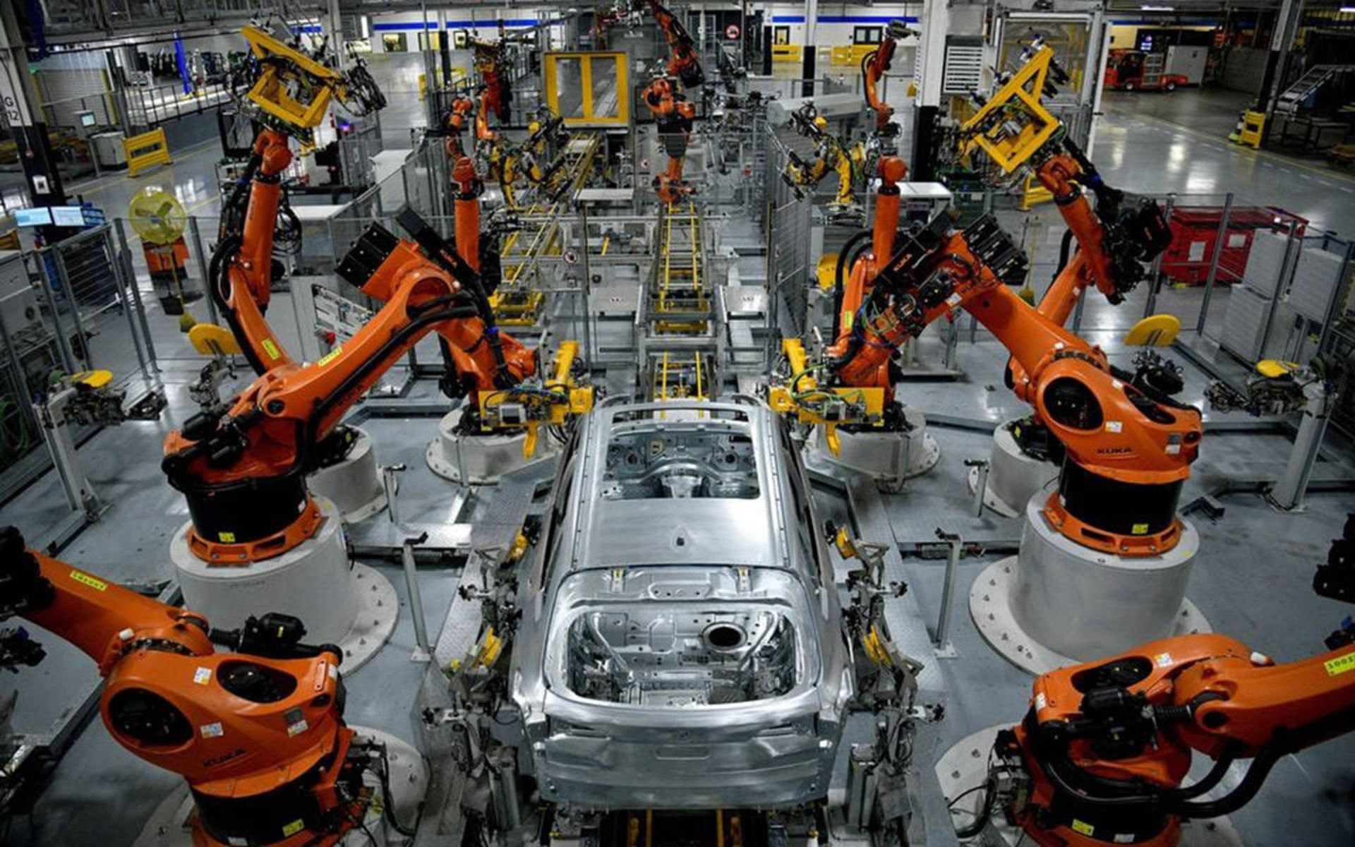 نمایی از کارخانه‌ی خودروسازی بی‌ام‌و در کارولینای جنوبی - تصویر از خط اسمبلی که بدنه‌ی خودرو‌ها در وسط هستند و بازوهای رباتیک اسمبلی نارنجی رنگ در دو سمت خط تولید. 