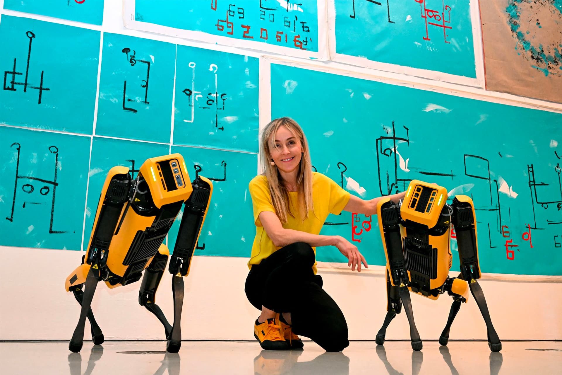 یک زن با لباس زرد در کنار دو سگ رباتیک