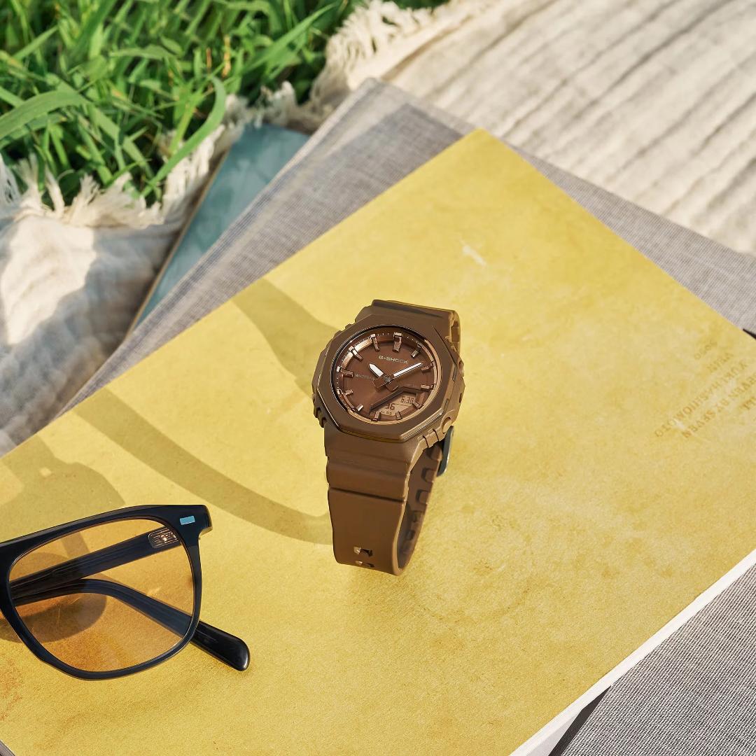 ساعت مچی جی‌شاک (Casio G-Shock) مدل GMA-P2110B با بدنه قهوه‌ای روی کتاب
