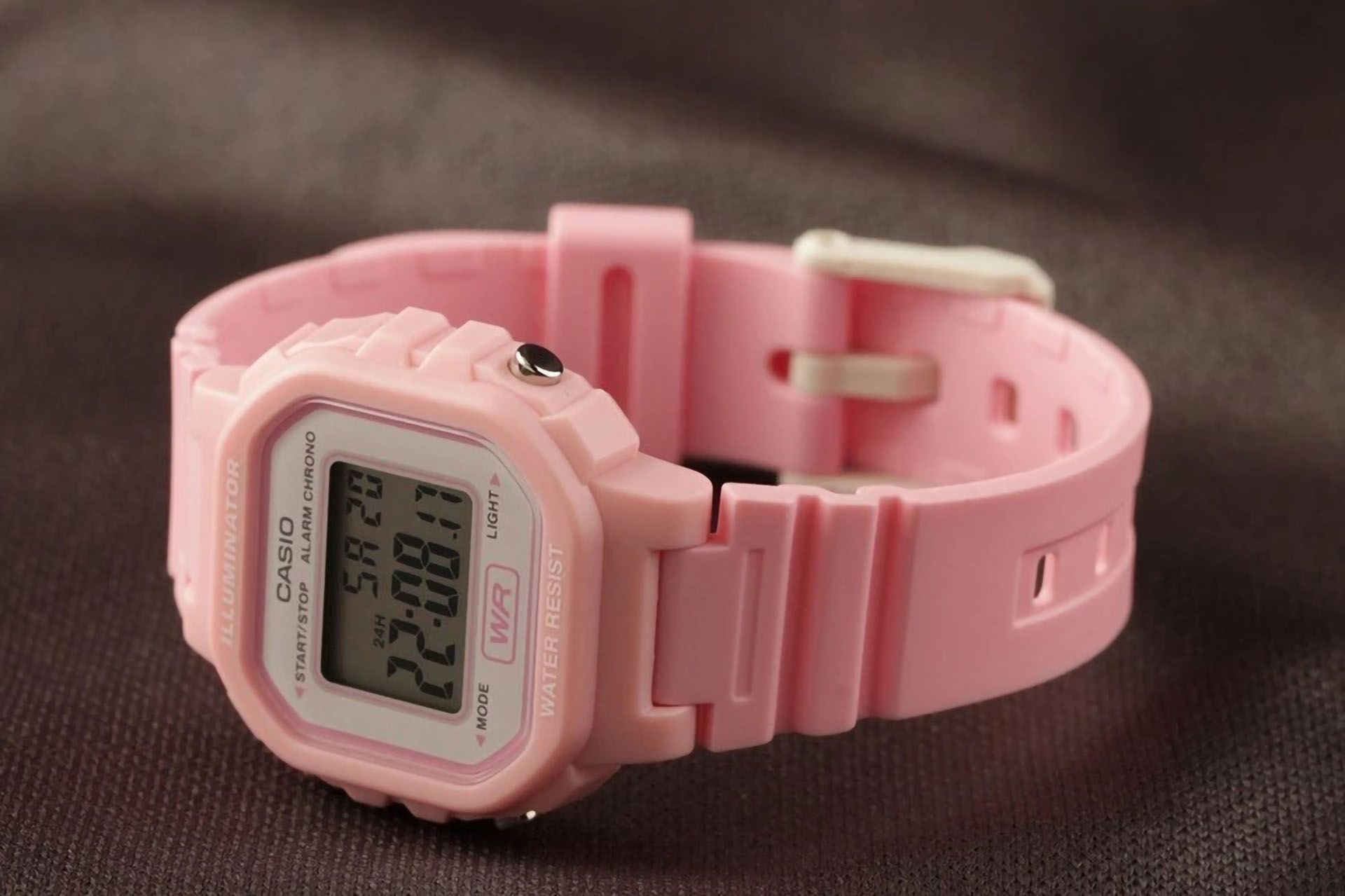 ساعت مچی دیجیتال بچگانه کاسیو مدل la 20wh صورتی رنگ نمای کامل ساعت روی پارچه قهوه‌ای