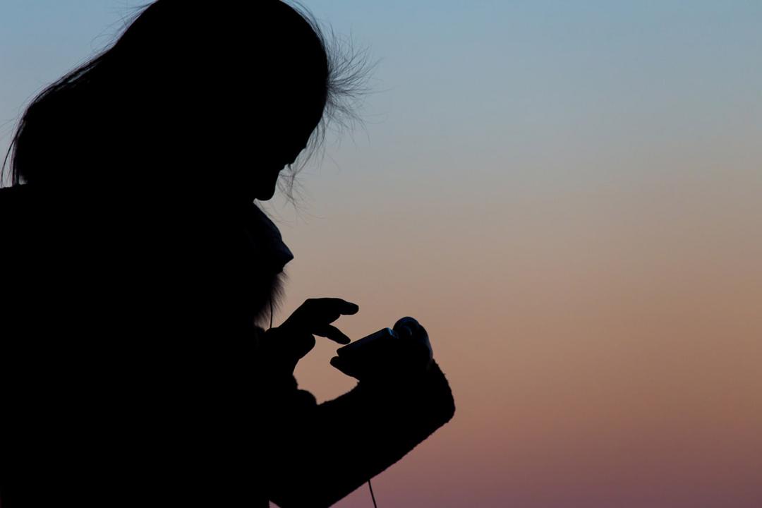 سایه کودک در حال کار با گوشی هوشمند در هنگام غروب