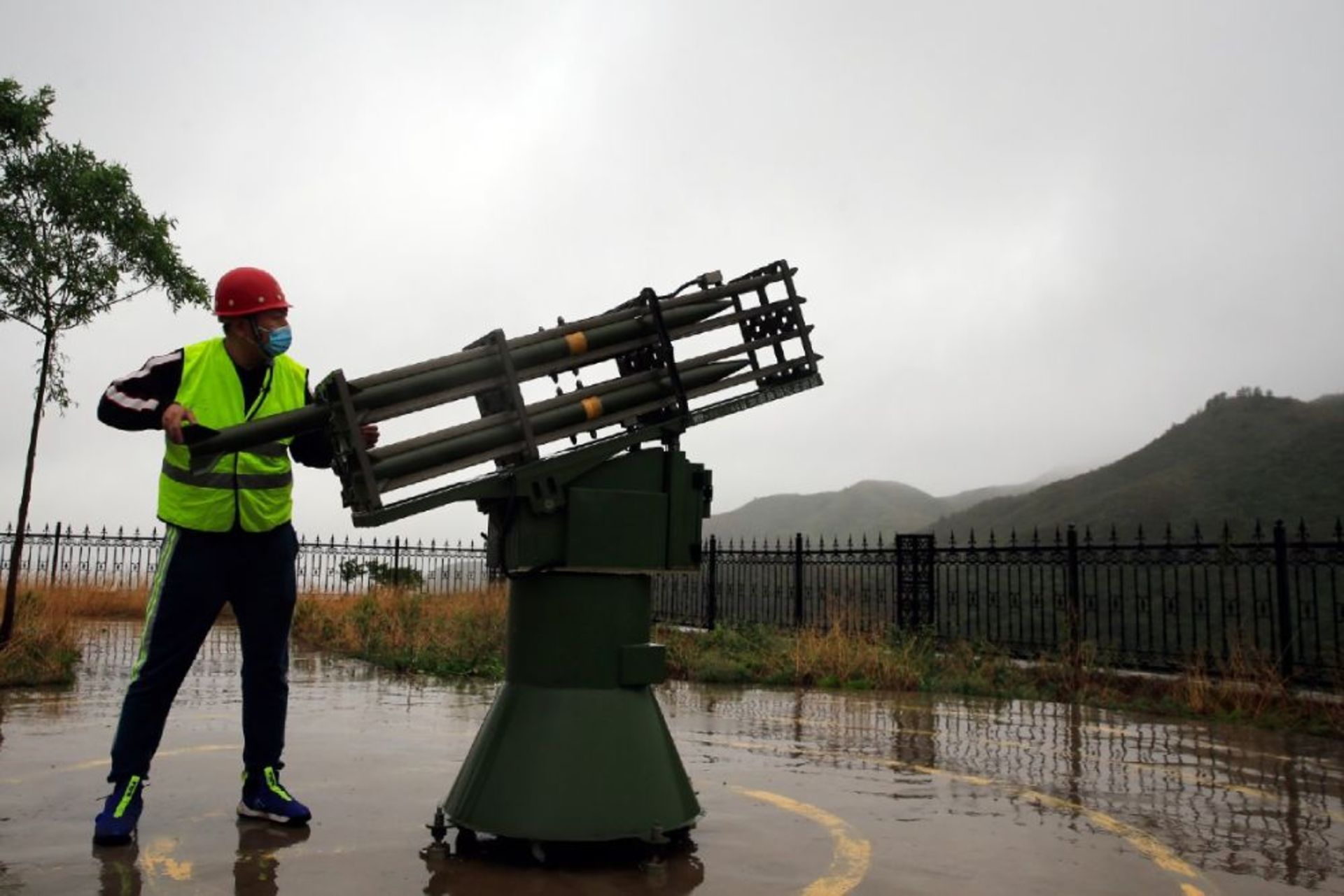 مرد با کت زرد و کلاه ایمنی قرمز در کنار موشک‌انداز ایستاده و در حال بارگیری موشک است.
