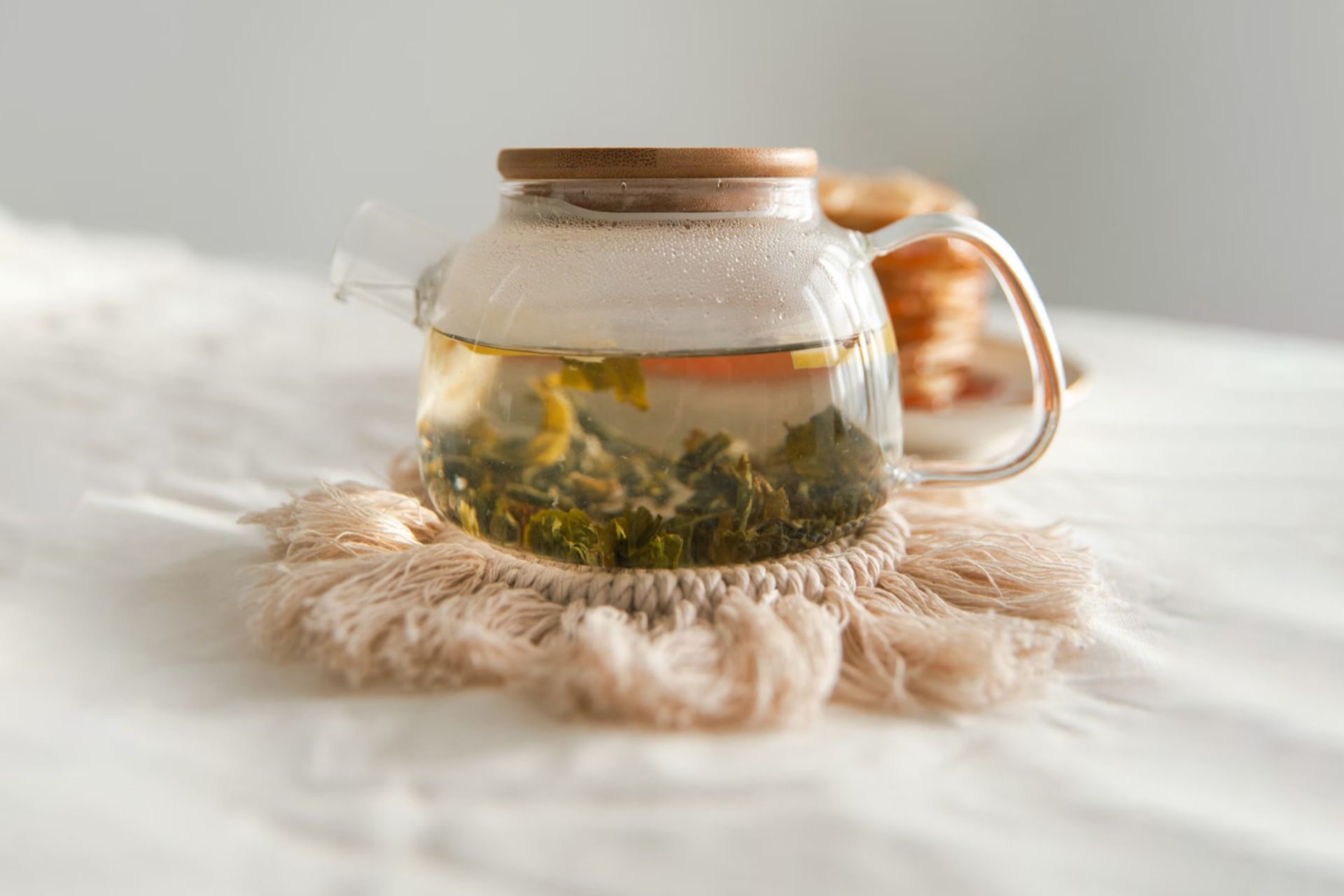 قوری شیشه‌ای شفاف از چای سبز روی پارچه سفید
