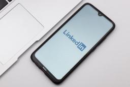 لوگوی لینکدین در صفحه نمایش یک گوشی هوشمند در کنار لپ‌تاپ