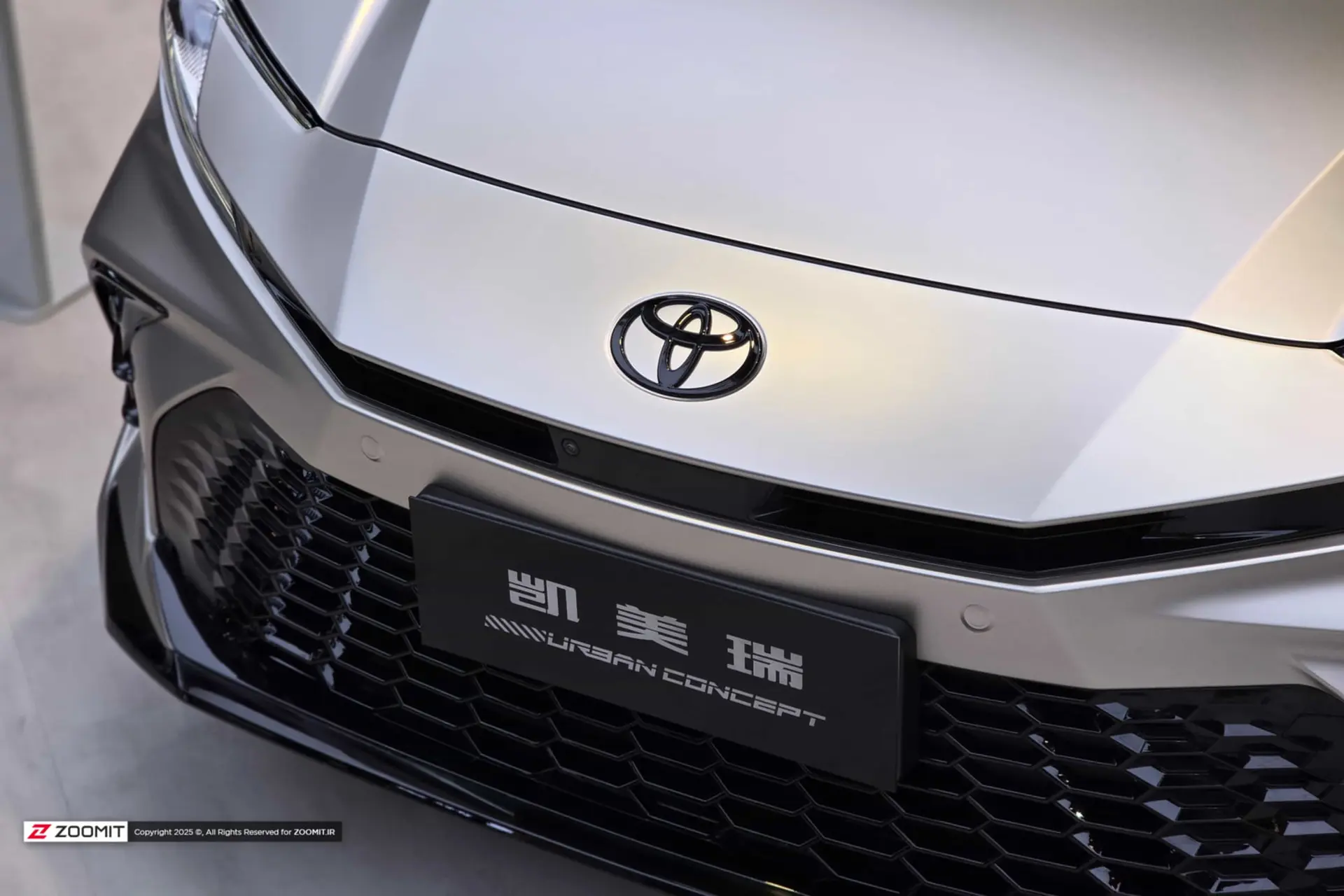 لوگوی برند تویوتا (Toyota) روی بدنه نقره‌ای خودروی هیبریدی