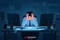 مردی مستاصل پشت میز کار در میان دو مانیتور کامپیوتر