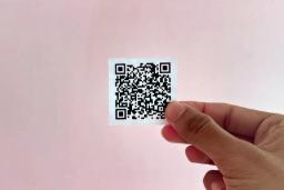 کد QR (QR Code) کوچک روی یک کاغذ سفید در دست
