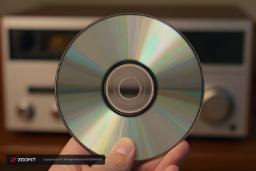 قرص سی‌دی (Compact Disc) در دست یک فرد در مقابل دستگاه پخش موسیقی