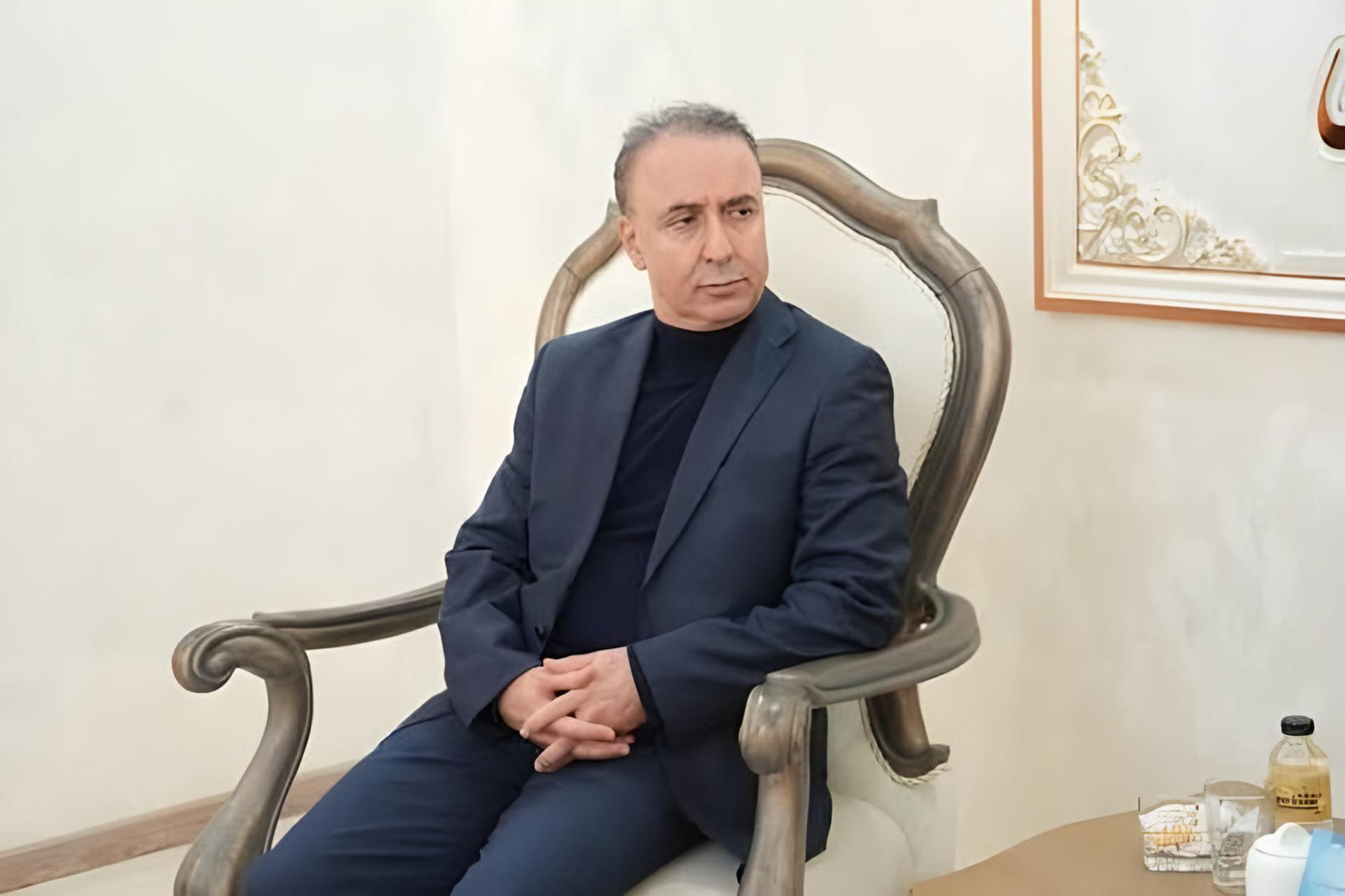 مردی با کت و شلوار تیره روی یک صندلی کلاسیک نشسته است