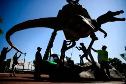 مجسمه بزرگ دایناسور (Dinosaur) در حال جابجایی توسط کارگران با جرثقیل