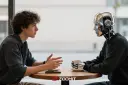 مرد جوان در حال گفت‌و‌گو با یک ربات انسان‌نما (Humanoid Robot) پشت میز کافه