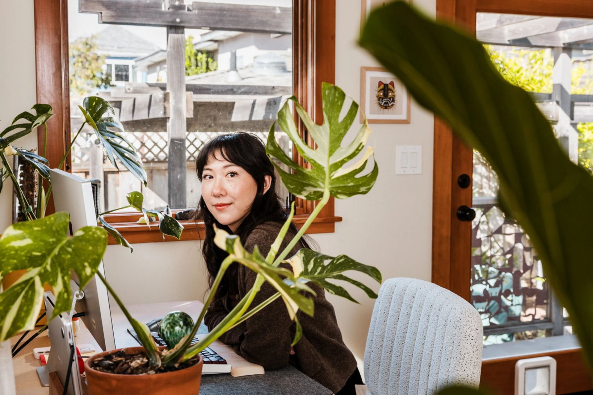 دختری با لبخند پشت میز کامپیوتر  پشت گلدان