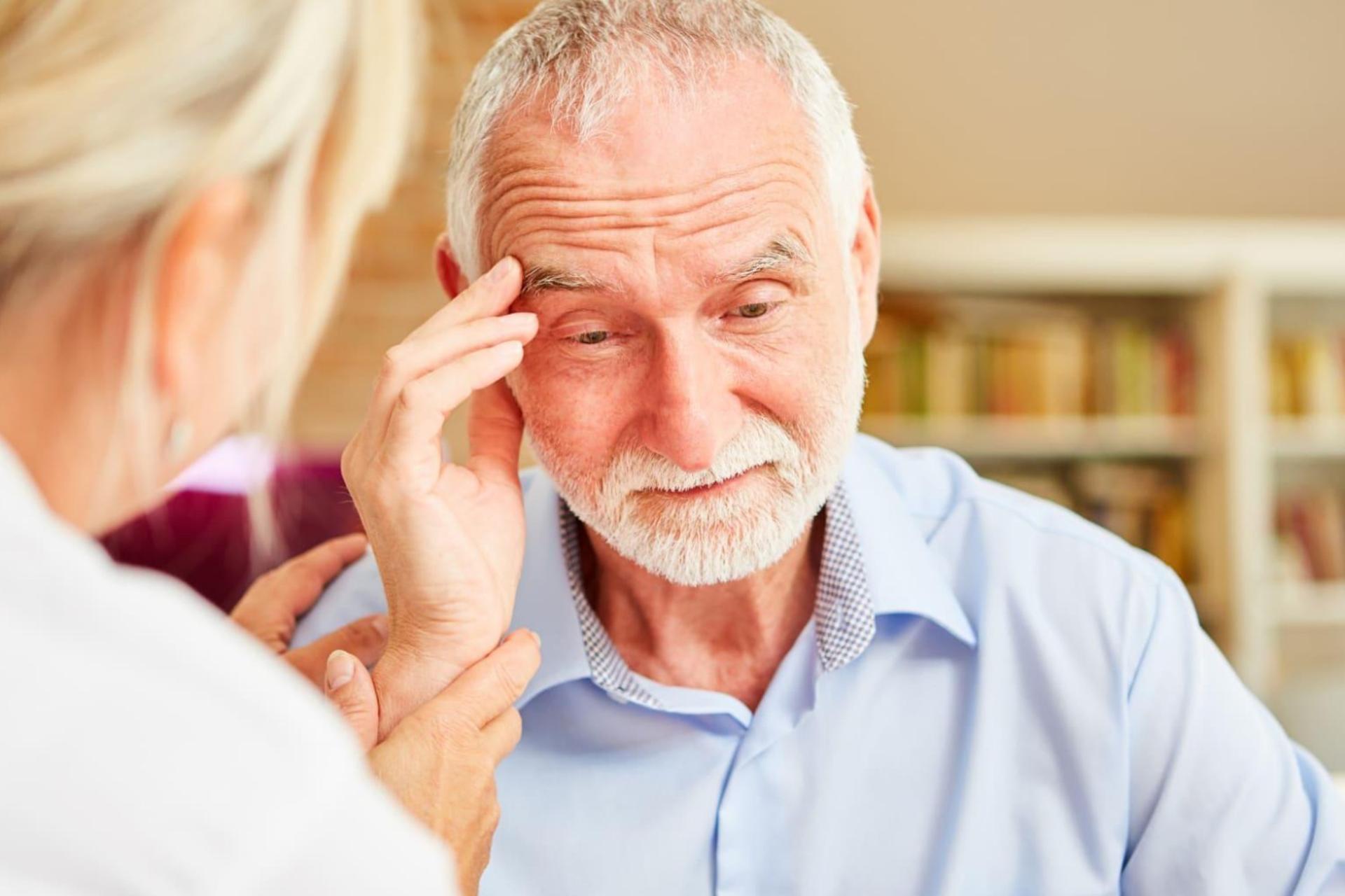 پیرمرد مبتلا به آلزایمر دستش را روی سر گذاشته و مقابل پزشک نشسته است.