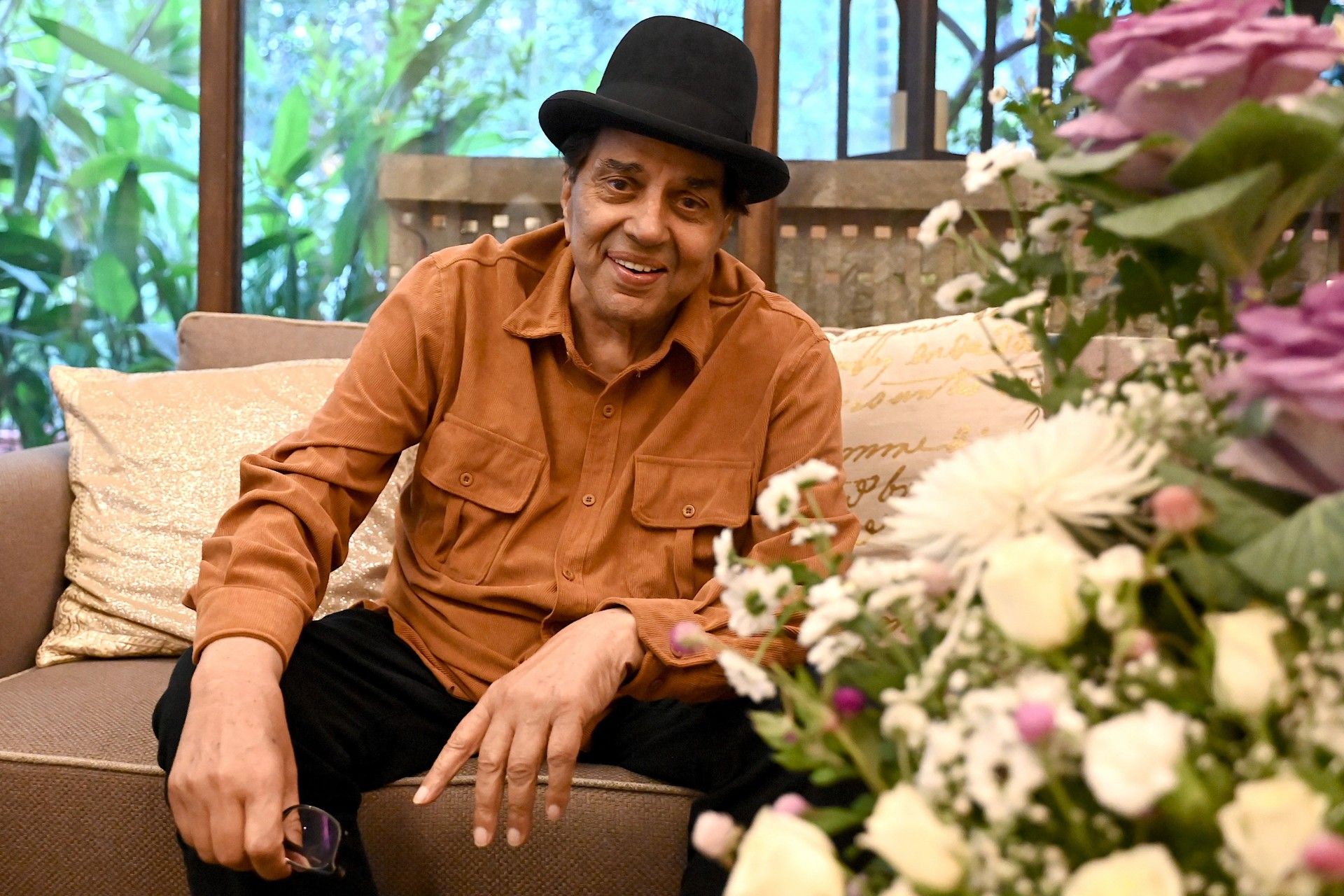 چهره‌ی مرد مسن با کلاه نشسته روی صندلی کنار گل