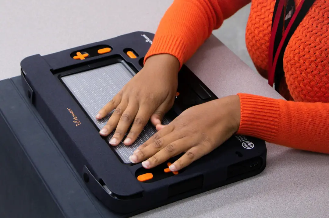 دست‌های فردی روی دستگاه خواندن خط بریل (Braille) دیجیتال