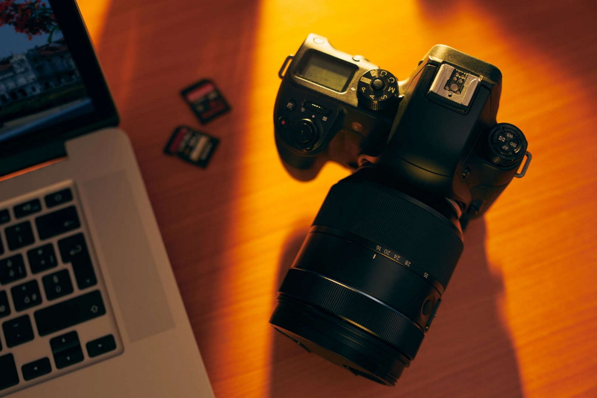 دوربین دیجیتال و چند کارت حافظه کنار لپ تاپ روی میز