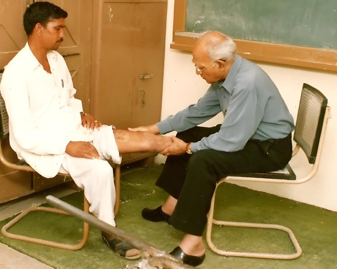 پزشک مسن در حال معاینه پای مردی که روی صندلی نشسته است