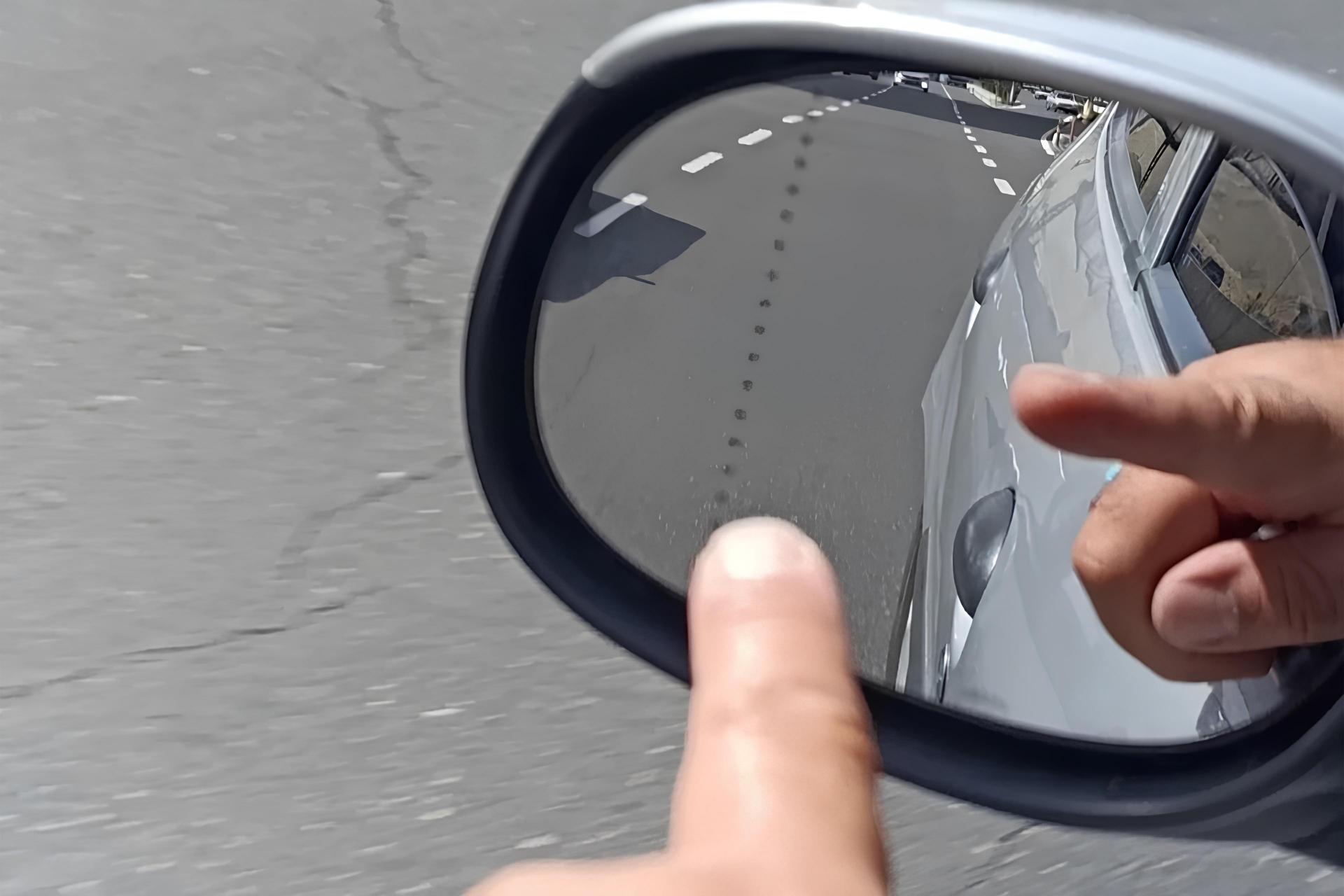 شخصی در حال اشاره به نقطه‌چین روی آینه‌ی جانبی ماشین