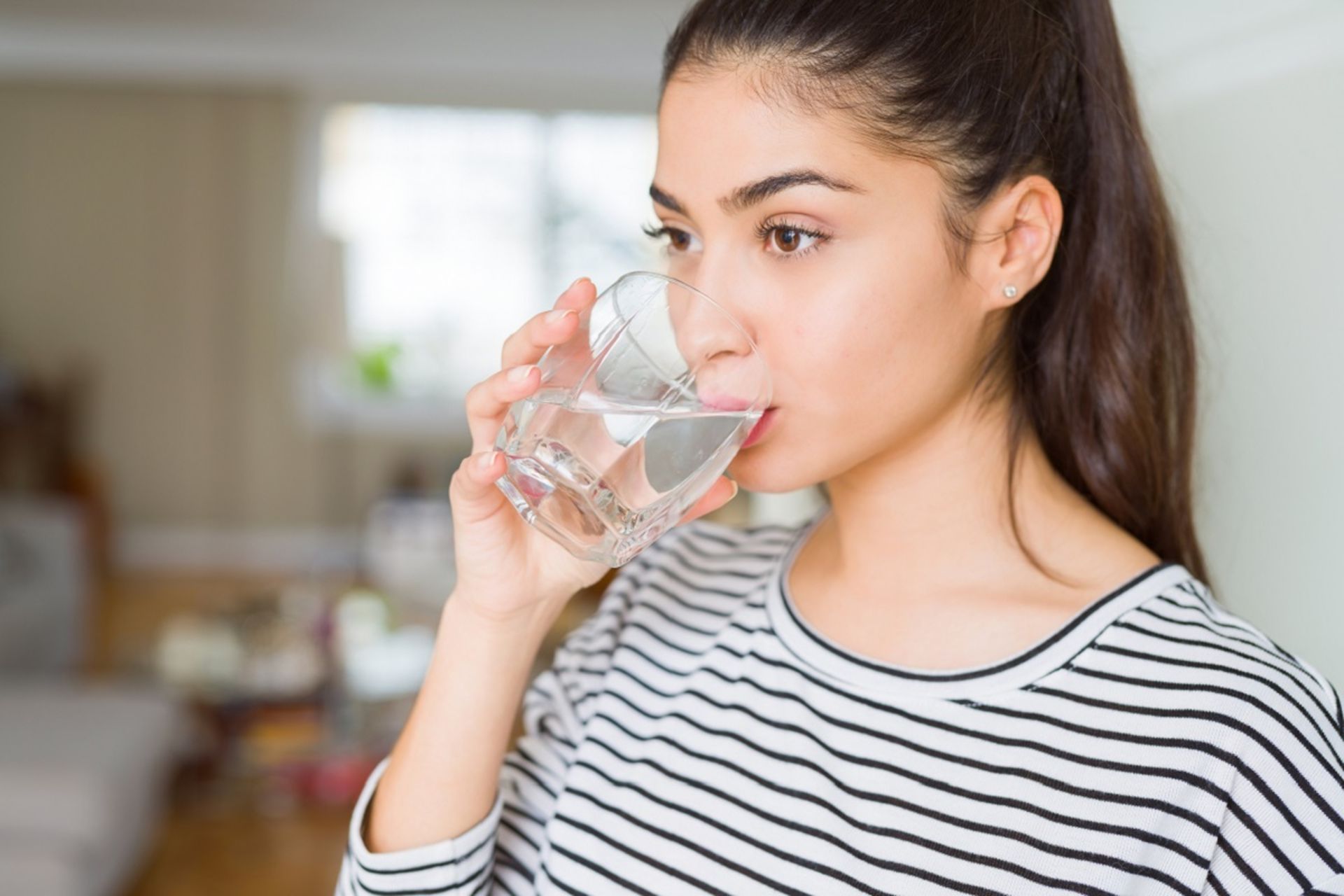دختر جوان درحال نوشیدن یک لیوان آب است