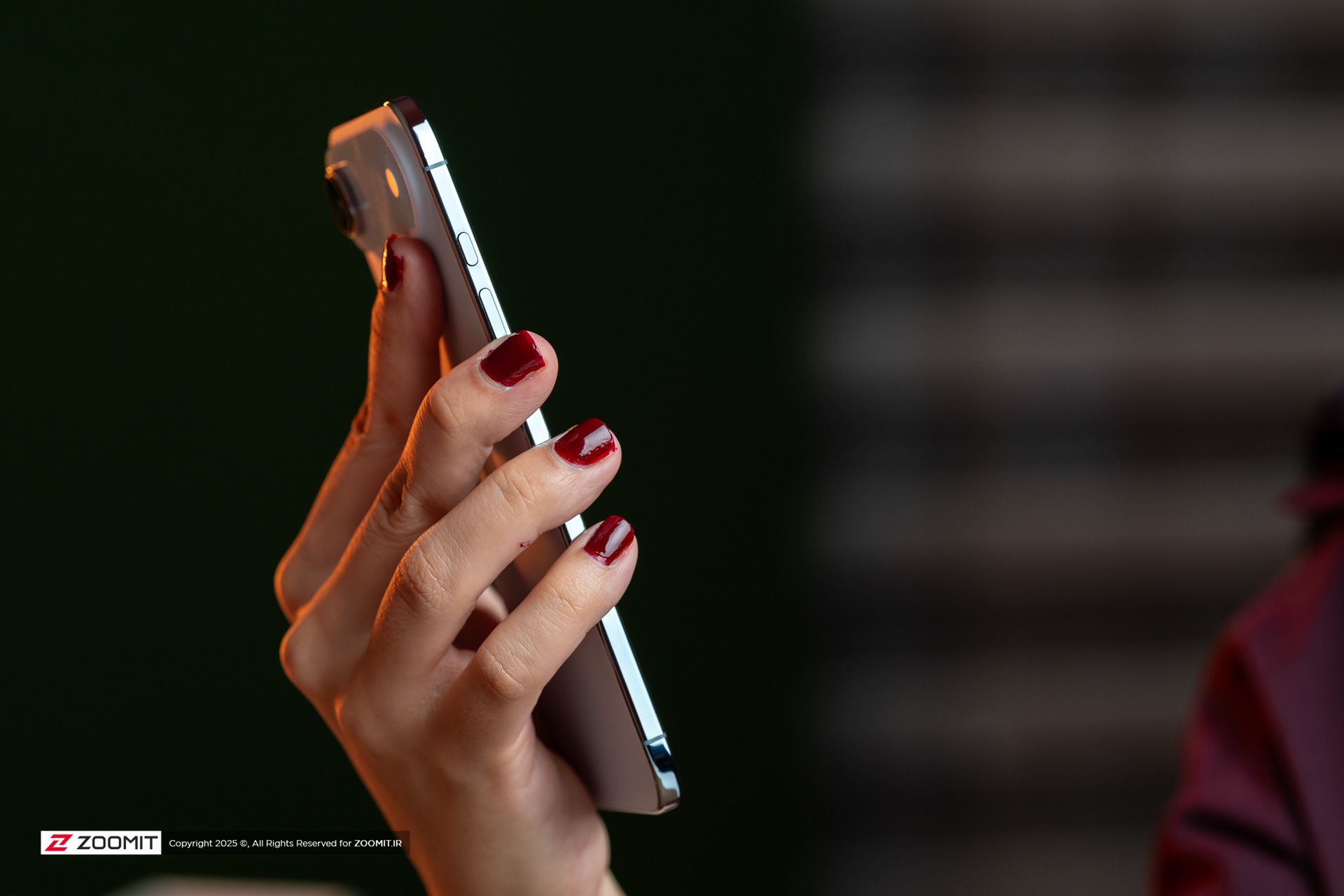 دست یک زن با لاک قرمز که یک آیفون ایر را از کنار نگه داشته و ضخامت کم آن را نشان می‌دهد