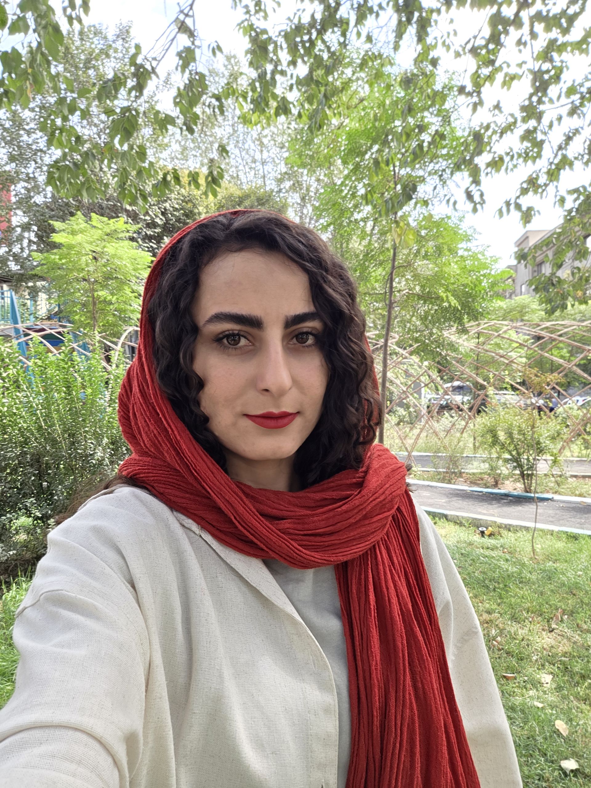 سلفی زن با روسری قرمز و لباس روشن در یک پارک در روز آفتابی