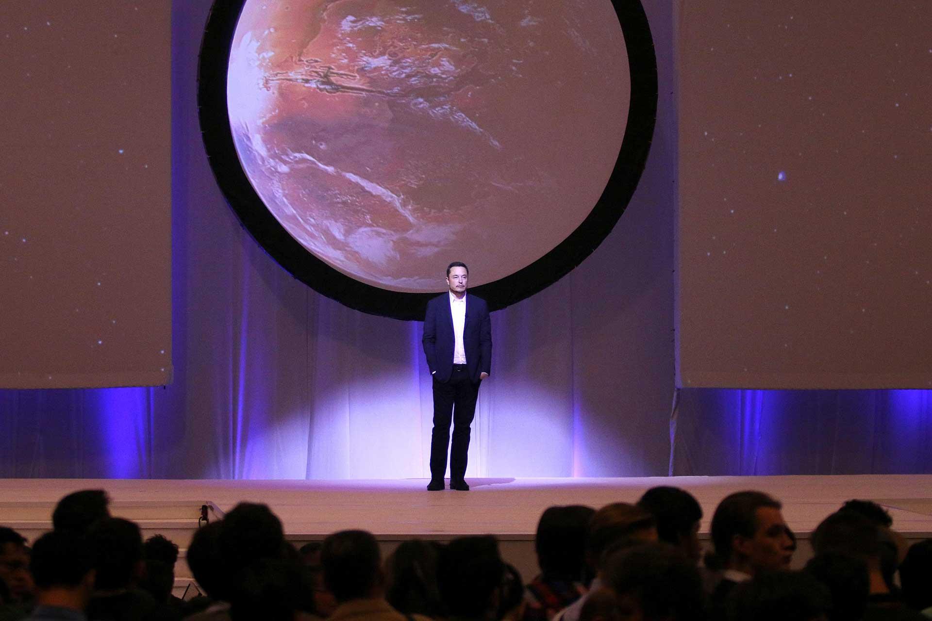 ایلان ماسک روبروی حضار روی استیج ایستاده و تصویر مریخ پشت سر او است