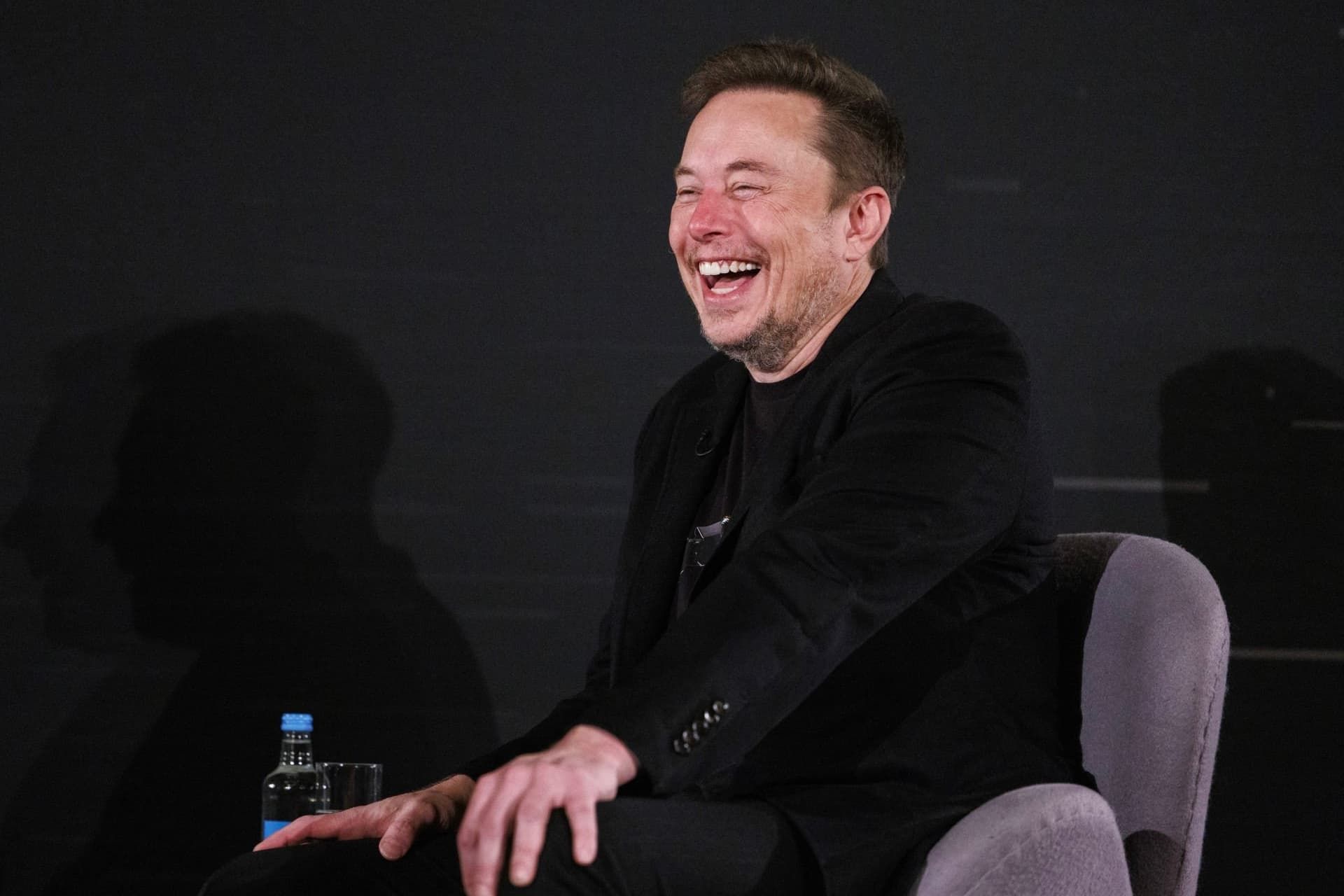 خنده ایلان ماسک / Elon Musk روی صندلی با لباس مشکی