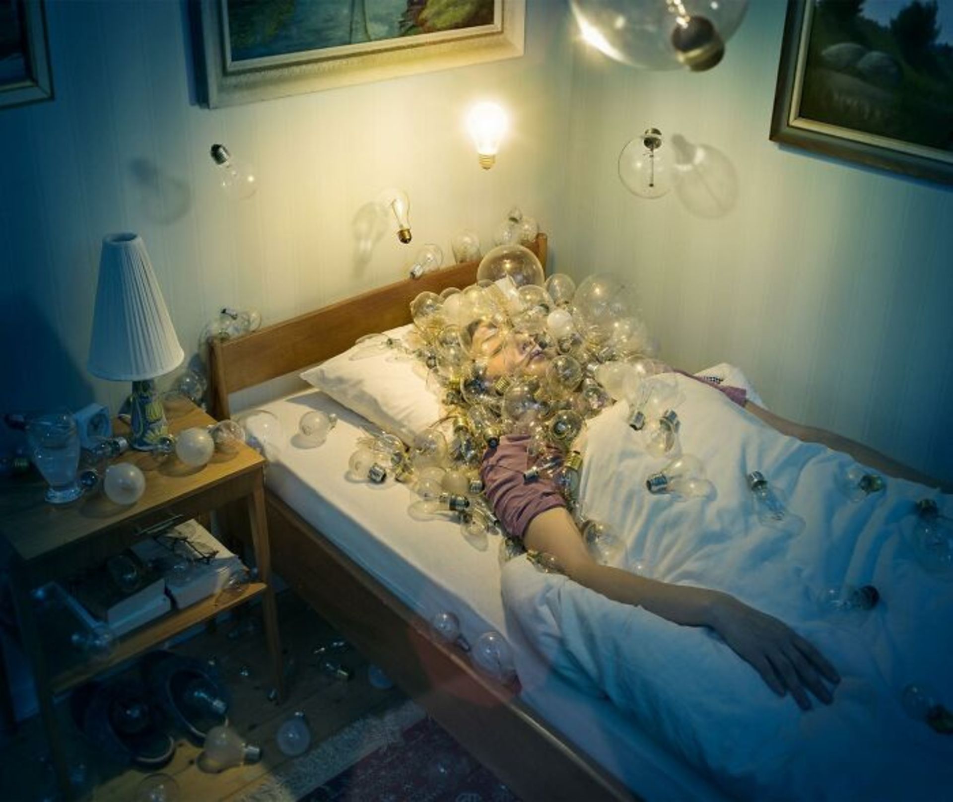 زن خوابیده روی تخت با سری پوشیده از حباب‌ های لامپ