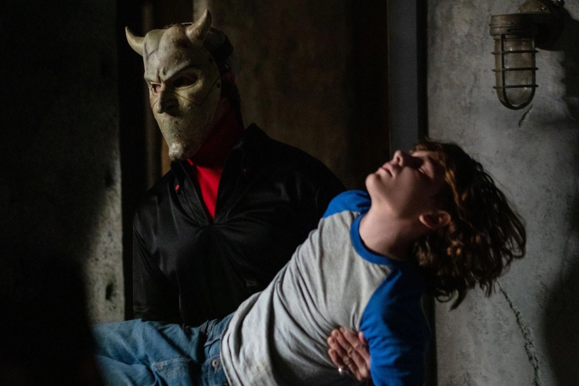 یک مرد با ماسک ترسناک در حال حمل کودک بیهوش روی دستانش