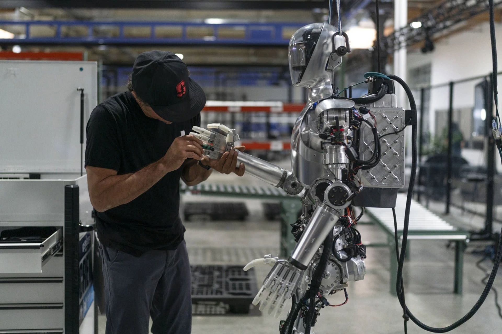 ربات انسان‌نمای شرکت فیگور از نمای کنار سمت چپ که یک مرد درحال کار کردن روی انگشتان دست آن است. 