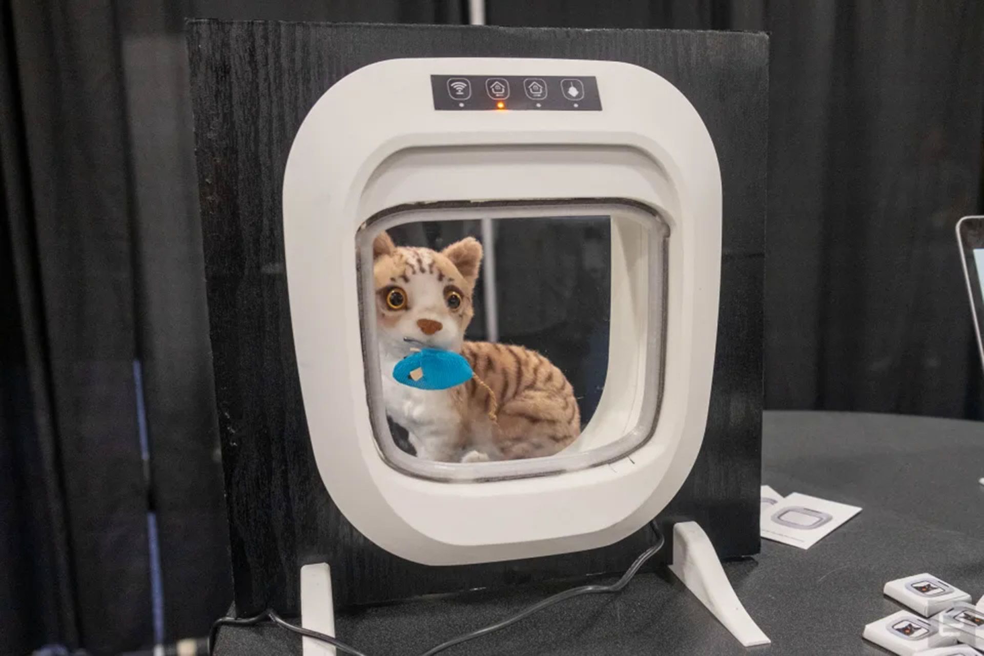 نمای واقعی از درب گربه‌ی Flappie در نمایشگاه CES 2024 که یک گربه‌ی عروسکی با یک موش عروسکی در دهانش بیرون آن مانده اند
