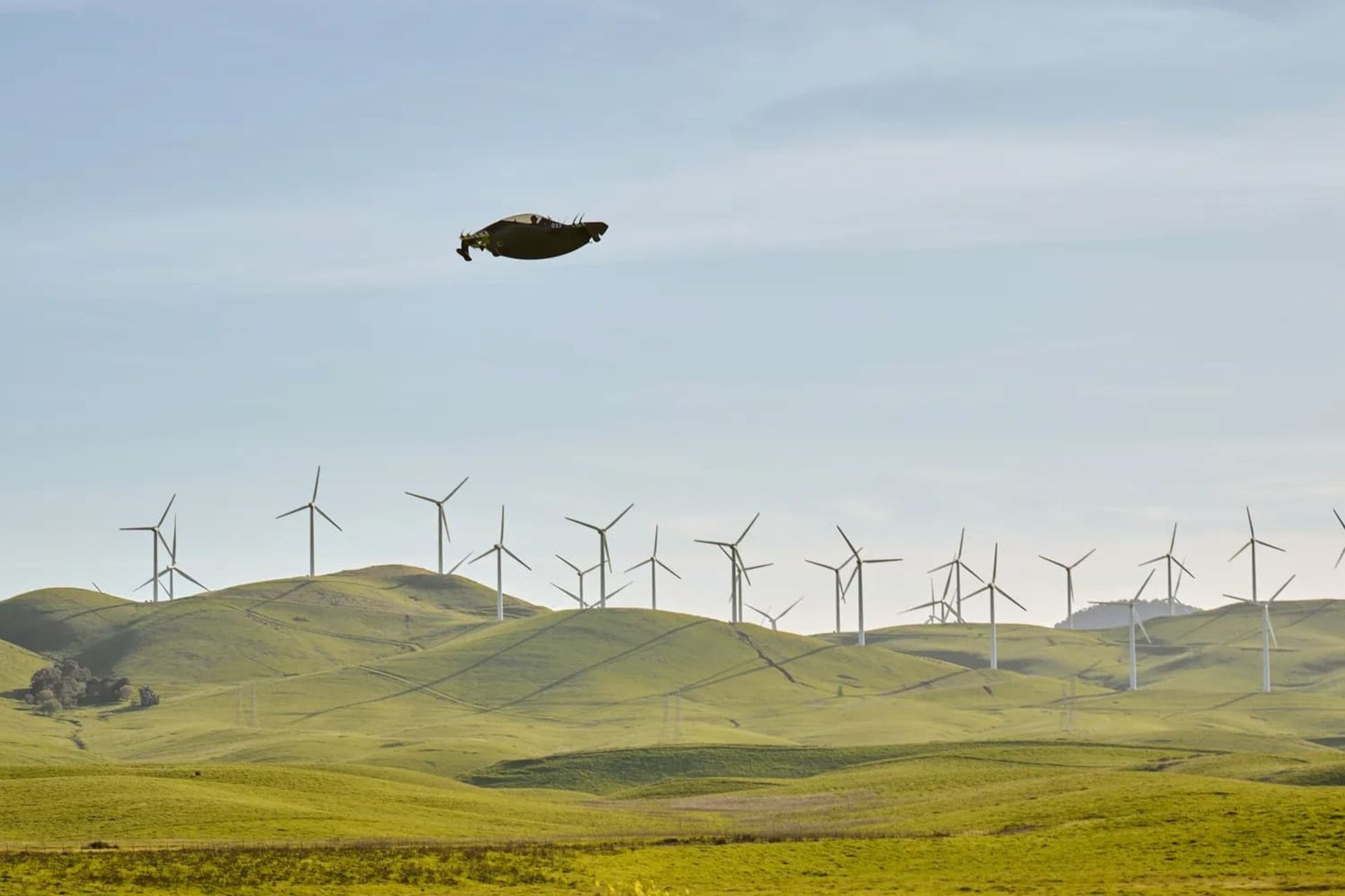 Small flying vehicle over a green land with wind turbines