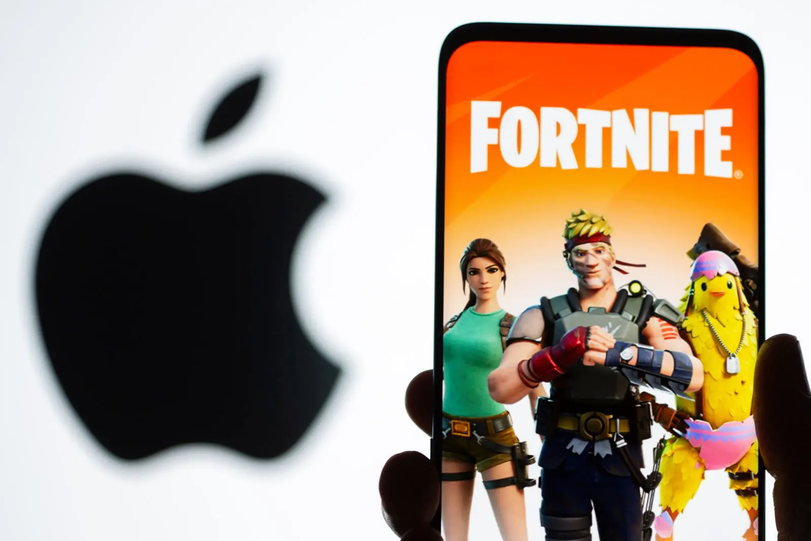 بازی فورتنایت روی صفحه‌نمایش یک گوشی هوشمند در کنار لوگوی اپل