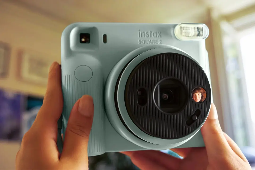 دوربین چاپ فوری اسکوئر ۲ (Instax Square 2) با بدنه رنگ آبی روشن در دست کاربر