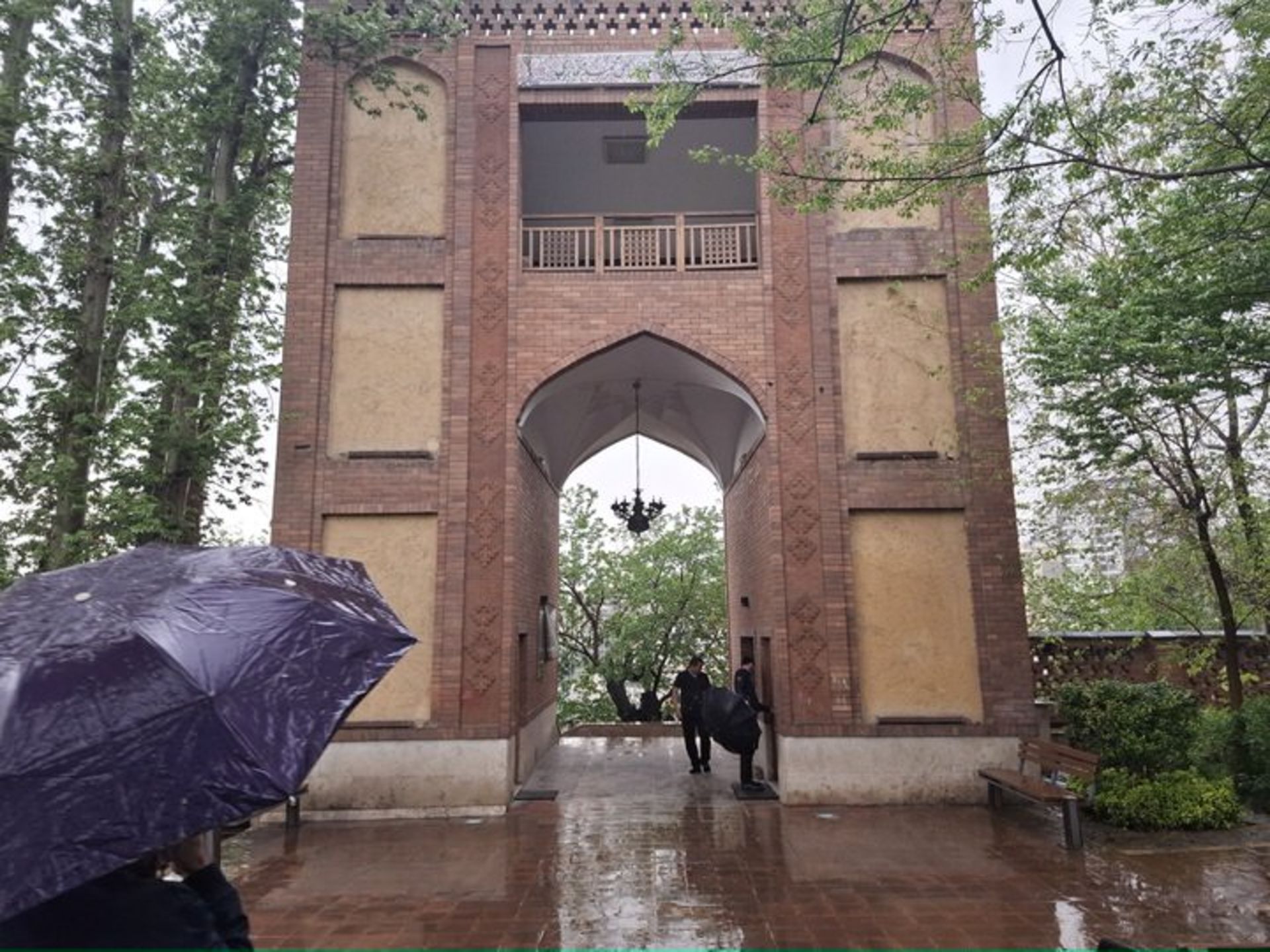 سردر آجری یک دروازه قدیمی در باغی با درختان سرسبز