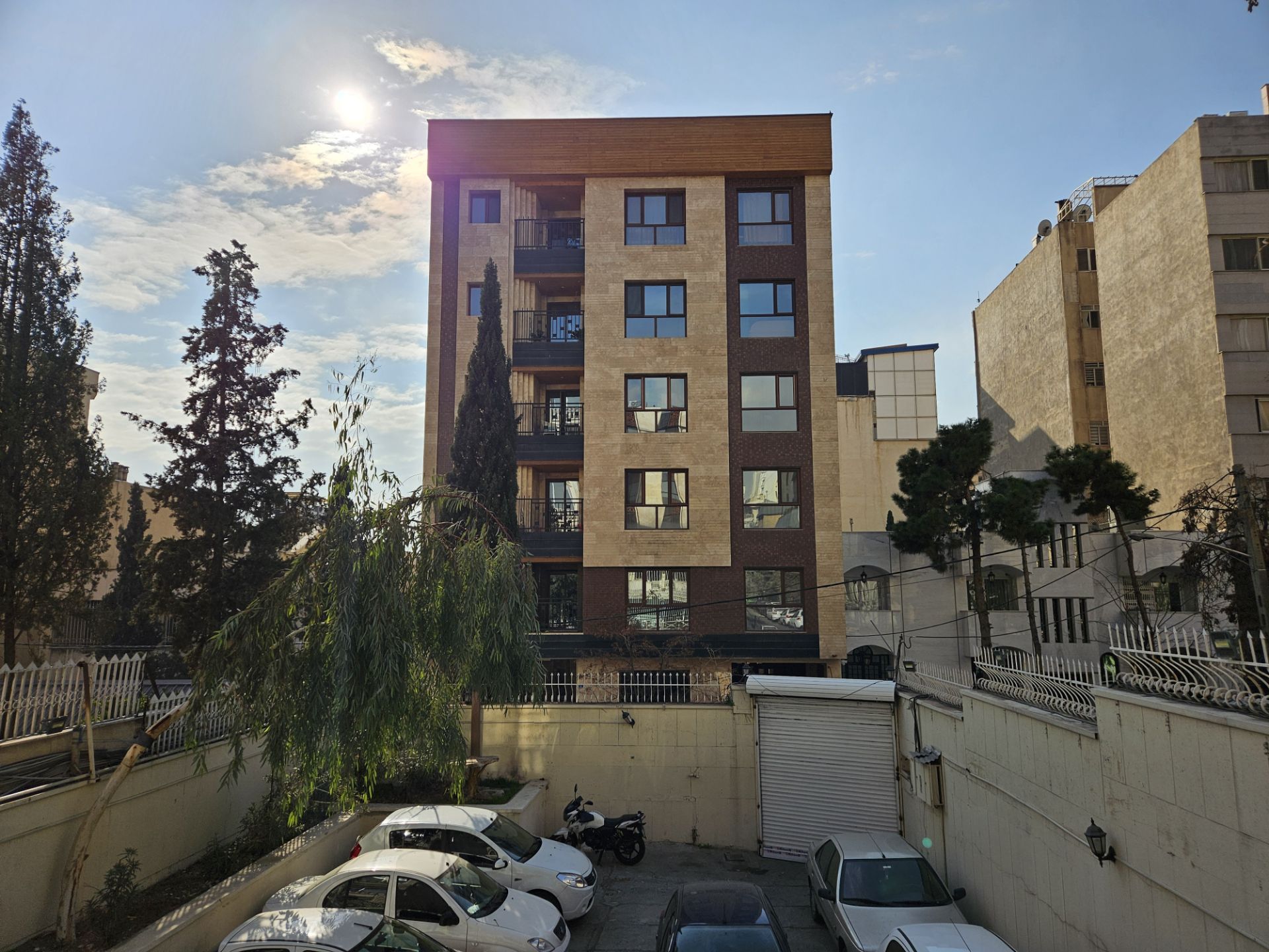 آسمان آفتابی با ساختمانی در روبرو و ماشین‌ها در پارکینگ